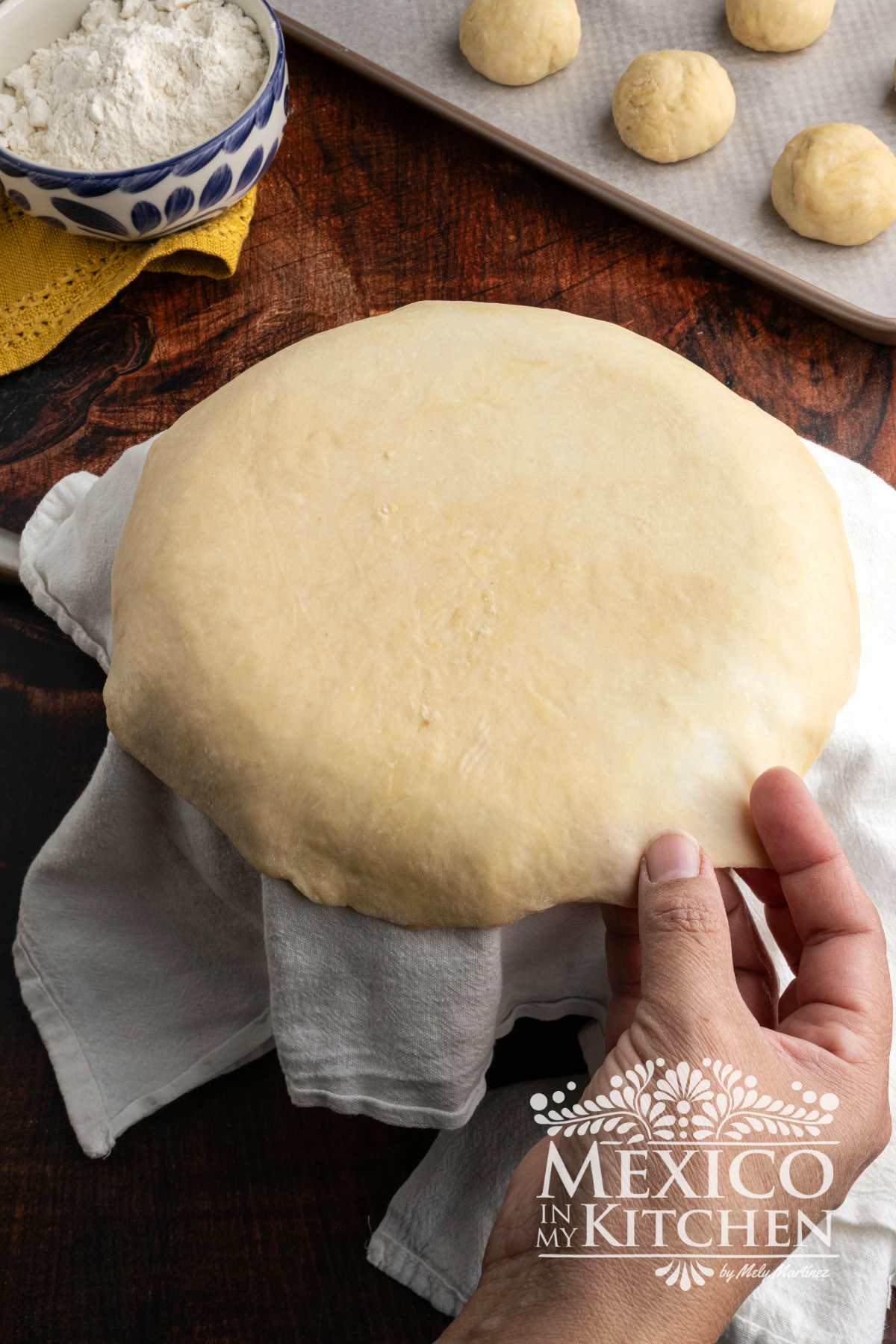Rolled out dough disk ove a pot cover with a kitchen towel.