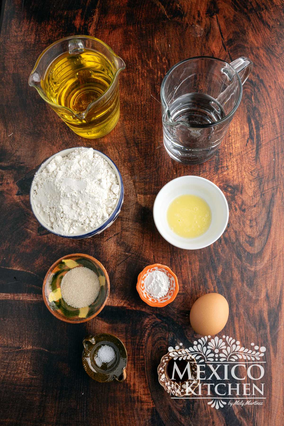 Oil, water, flour, butter, sugar, baking powder, one eggs and salt displayed over a table.