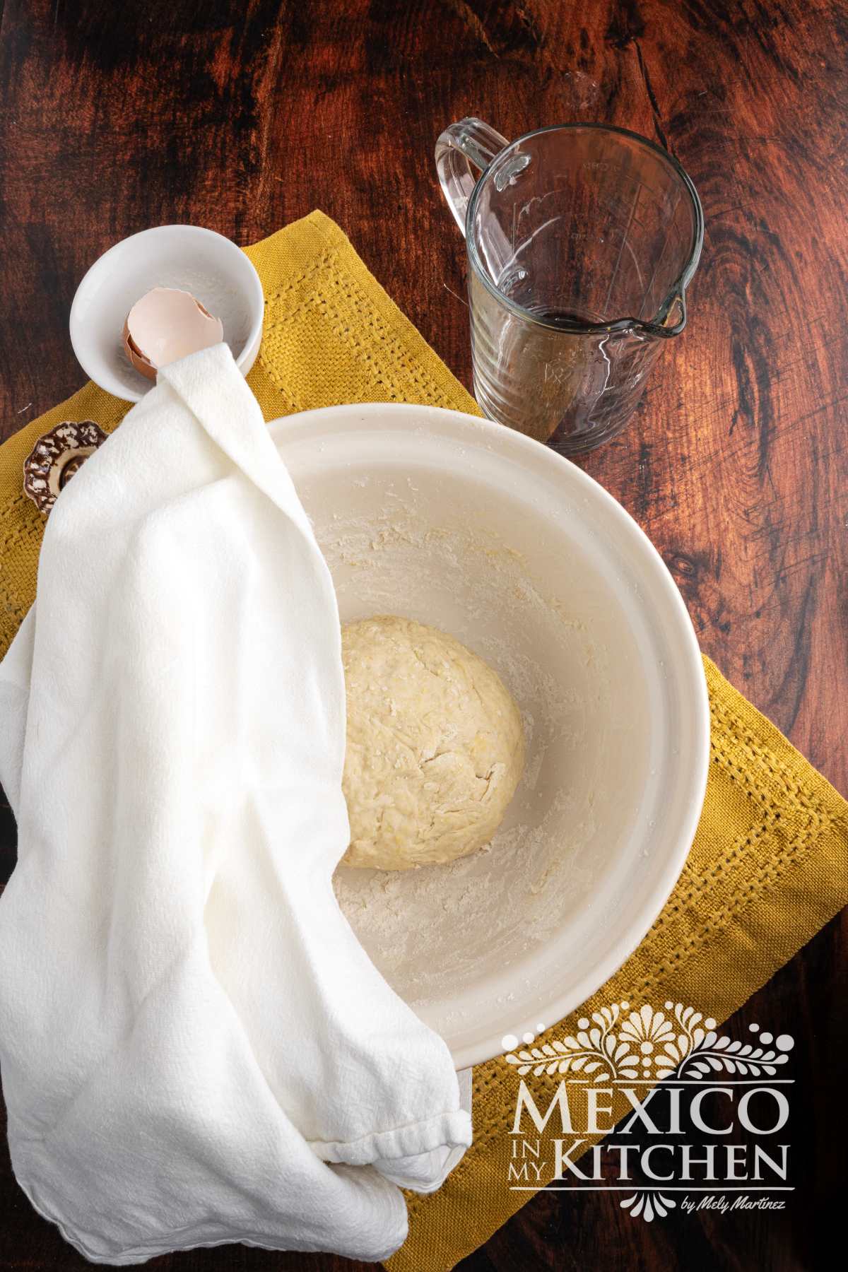 Dough resting in mixing bowl covered with a kitchen towel.