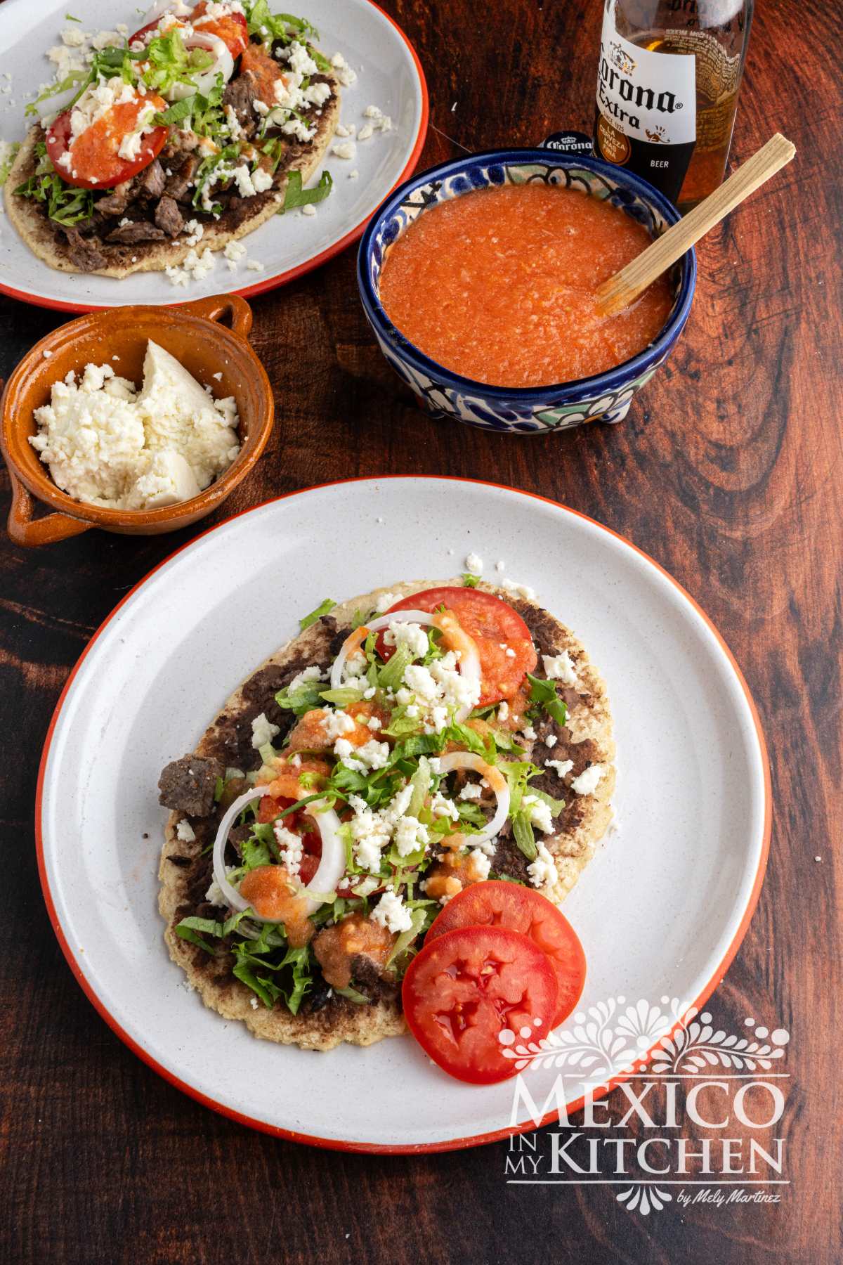 Mexican huarache recipe topped with beans, beef, queso fresco, lettuce, slices of onions and red salsa.