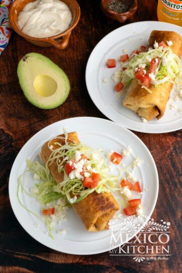 Shredded beef and potato chimichanga serve in a plate and topped with shredded lettuce, diced tomatoes, and queso fresco.