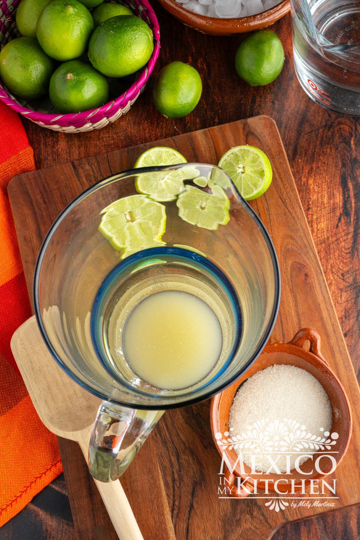 Mixing fresh lime juice with sugar in a glass pitcher.