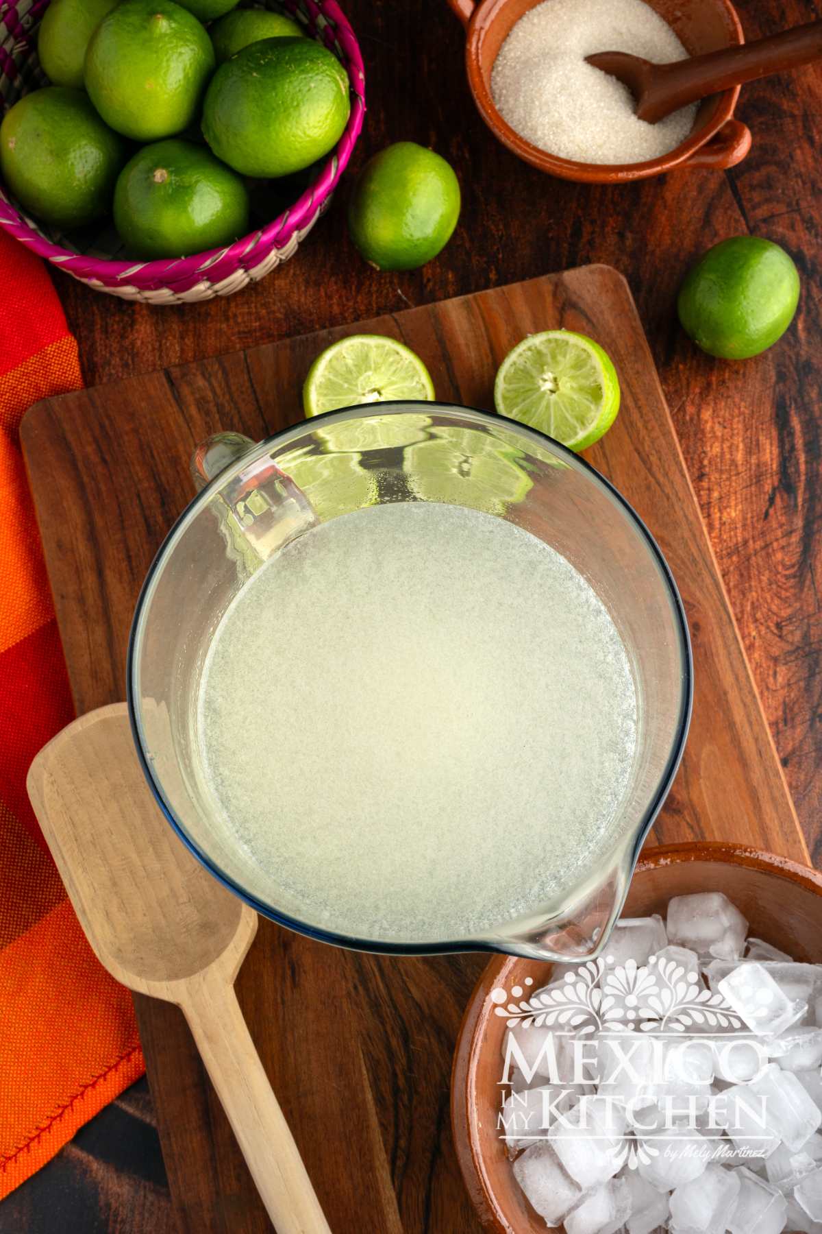 Mixing fresh lime juice, sugar, and water in a glass pitcher.