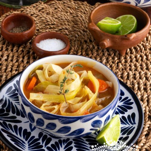 A bowl of cabbage soup, topped with a fresh thyme.