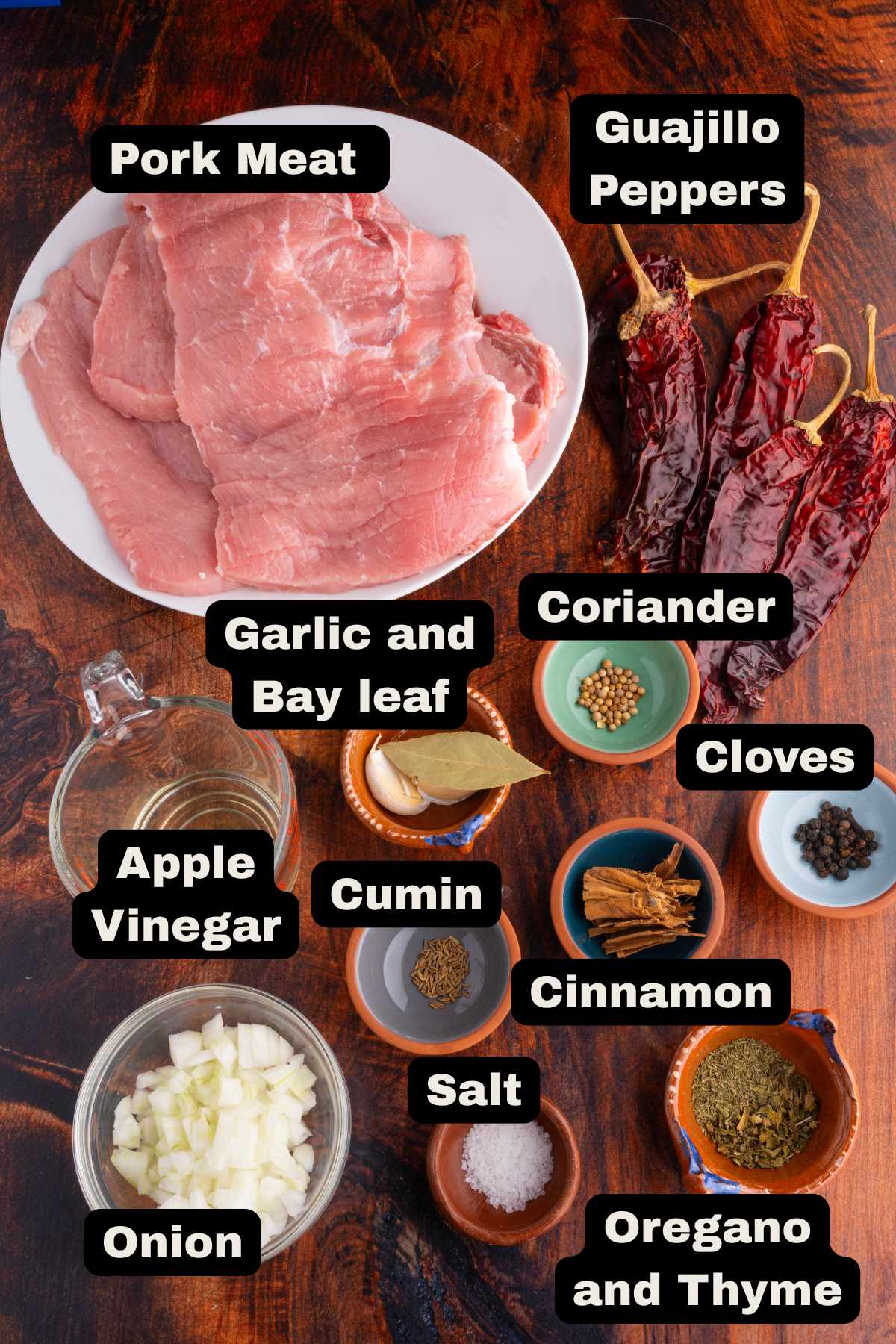 Ingredients to make carne enchilada, such as pork steaks, guajillo peppers, garlic, bayleaf, coriander, cloves, apple vinegar, salt, cinnamon, oregano and thyme.